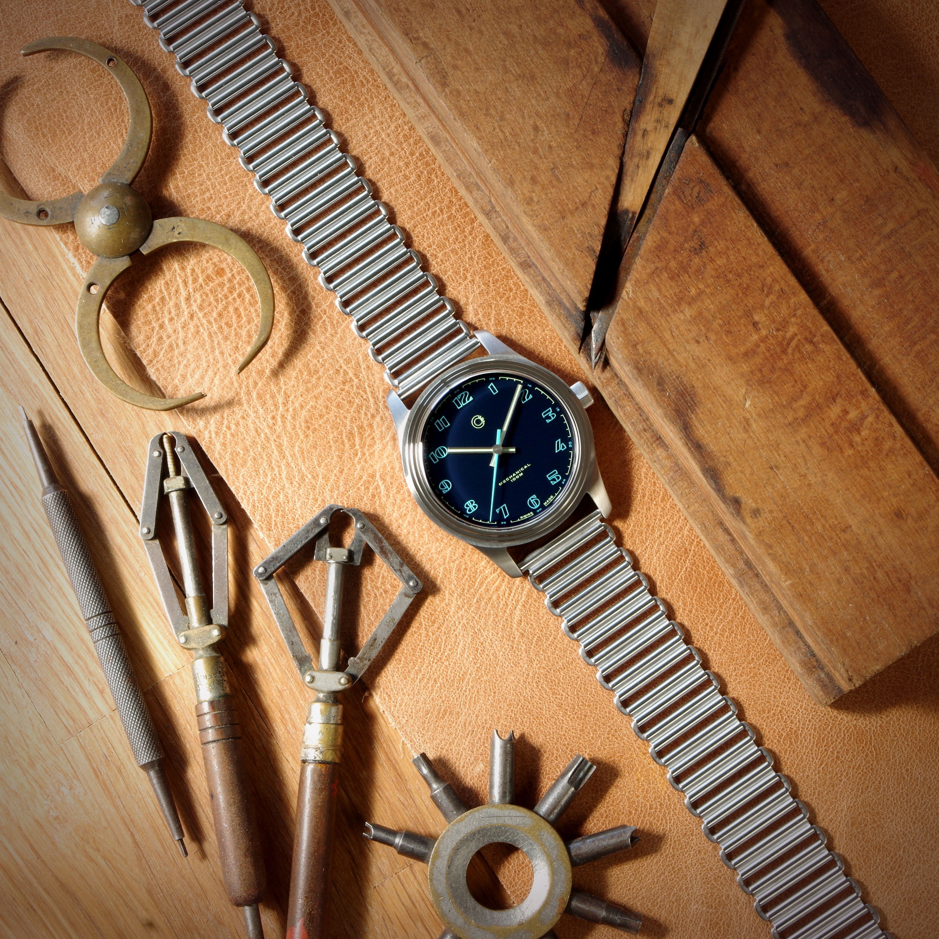 Photo of blue Camp Fieldtimer mechanical luxury Swiss Made vintage inspired dress field watch for men and women with colorful lacquer enamel dial designed in Los Angeles, California surrounded by antique watchmaking tools